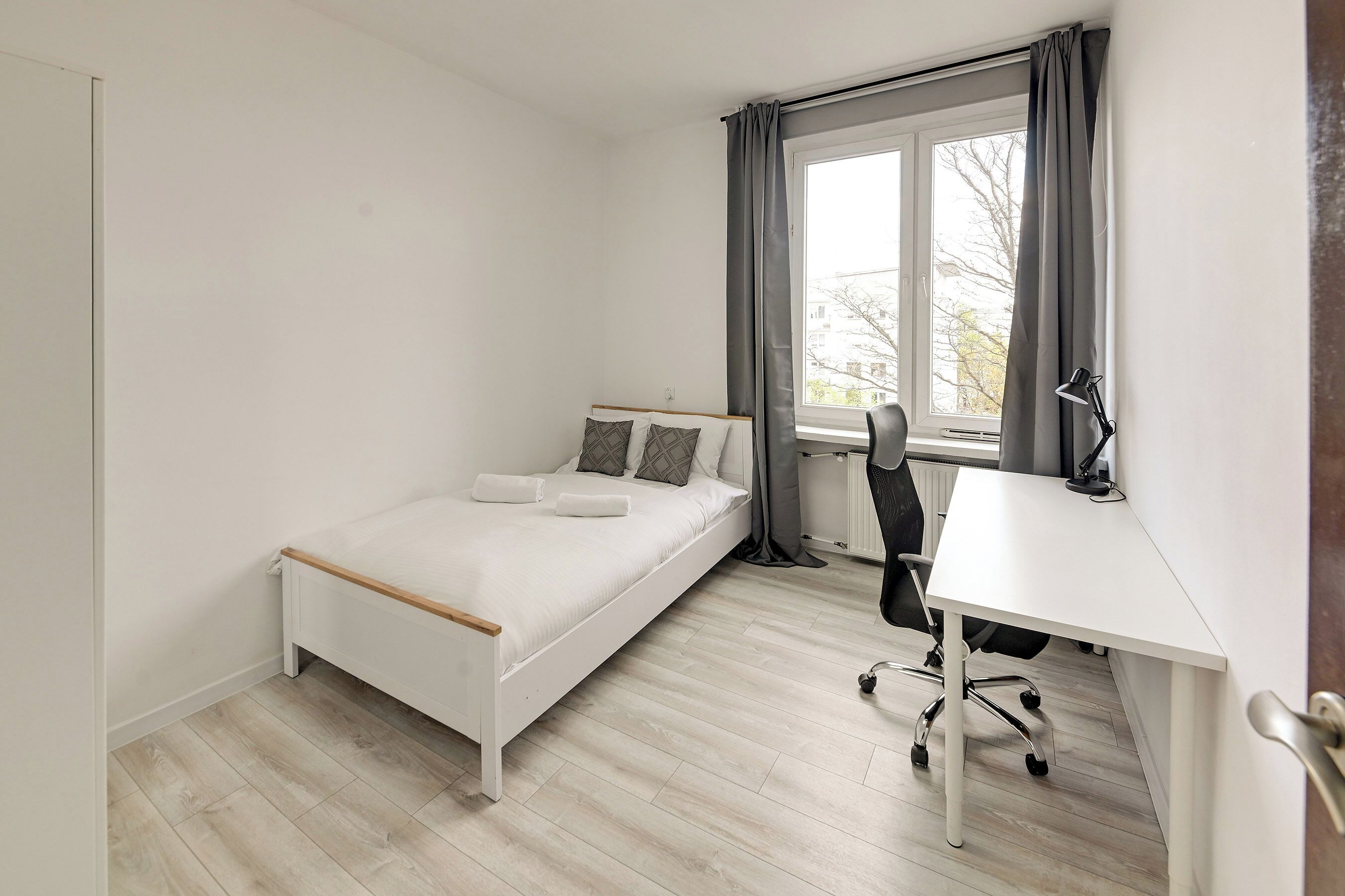 A bedroom with a bed, a desk, and a window with curtains.
