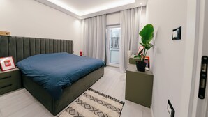 Een moderne slaapkamer met een bed, nachtkastje, gordijnen, een plant in pot en een raam met jaloezieën.