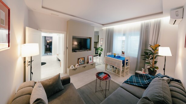Een moderne woonkamer met een bank, een televisie, een eettafel en een keuken op de achtergrond.