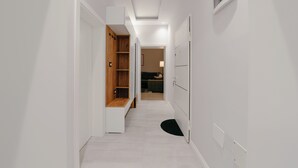 Een smalle gang met witte muren, een houten plankenwand, een zwart vloerkleed en een deur naar een andere kamer.