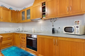 A kitchen with wooden cabinets, a microwave, a stove, and a sink. - Solar do Diabrete T2 – Spacious Apartment with Sea Views in Central Nazaré (Nazaré)