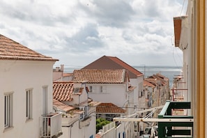 A narrow street with terracotta-tiled buildings, balconies, and a view of the sea. - Solar do Diabrete T2 – Spacious Apartment with Sea Views in Central Nazaré (Nazaré)