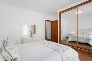A bedroom with a bed, a dresser, a mirror, and a large mirror reflecting the room. - Solar do Diabrete T2 – Spacious Apartment with Sea Views in Central Nazaré (Nazaré)