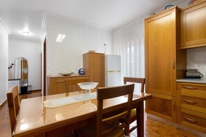 Ein Essbereich mit Holztisch und -stühlen, einem weißen Kühlschrank, Holzschränken und einer gefliesten Spritzschutzwand.