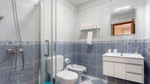 Ein Badezimmer mit Duschkabine aus Glas, Toilette, Bidet, Waschbecken mit Spiegel und Handtuchhalter.