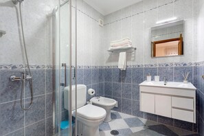 Ein Badezimmer mit Duschkabine aus Glas, Toilette, Bidet, Waschbecken mit Spiegel und Handtuchhalter.