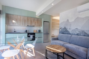 Una cocina moderna con mesa de comedor de vidrio, sillas de madera, un sofá gris y un mural de montaña.