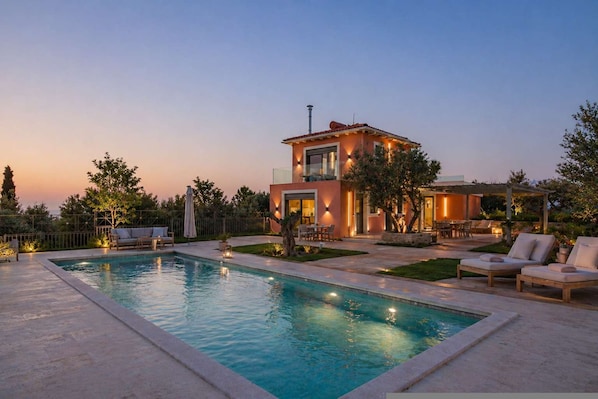 Una casa moderna con piscina, mobiliario exterior y una zona de patio bien iluminada.