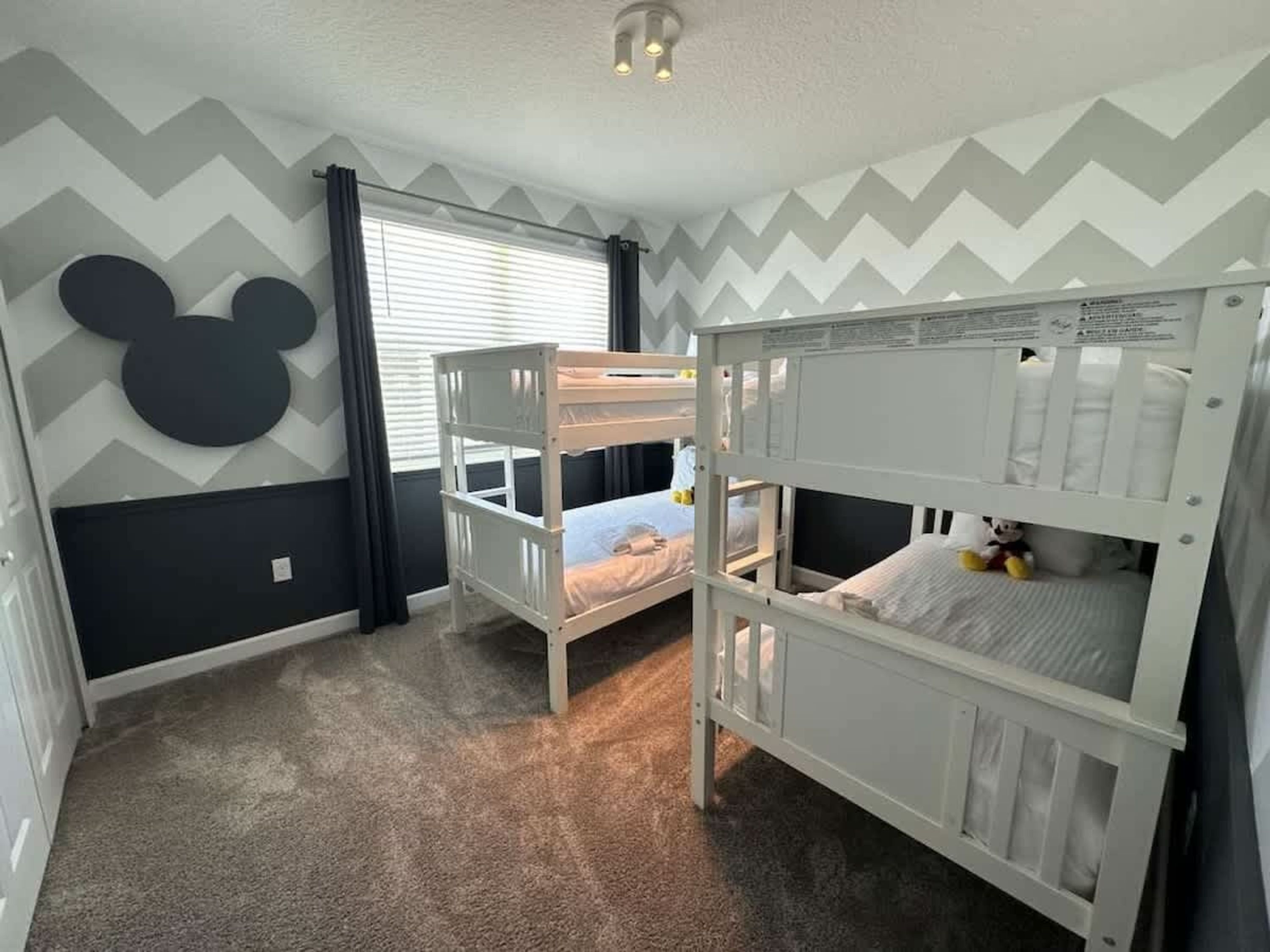 A room with two bunk beds, a Mickey Mouse wall decal, and a window with curtains.