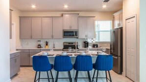 A modern kitchen with a central island, four blue chairs, and a stainless steel refrigerator. - Luxury 5BR Private Pool Disney Area (Kissimmee)