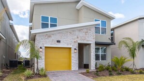 A modern two-story house with a stone facade, a yellow garage door, and a clear sky. - Luxury 5BR Private Pool Disney Area (Kissimmee)