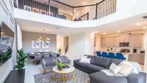 A spacious living area with a grey sofa, round coffee table, and a dining area with grey chairs. A kitchen with light-colored cabinets and a microwave is visible. - Luxury 5BR Private Pool Disney Area (Kissimmee)
