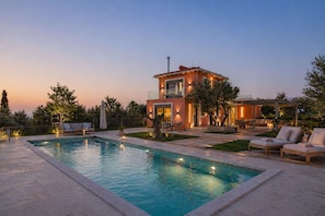Una casa moderna con piscina, mobiliario exterior y un patio bien iluminado.