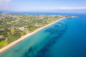 Vista aérea de una zona costera con playa, edificios residenciales y vegetación.