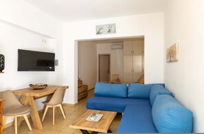 Una sala de estar moderna con una mesa de comedor de madera, un sofá azul y un televisor montado en la pared.