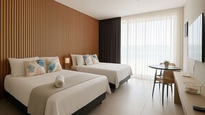 Ein Hotelzimmer mit zwei Betten, einem kleinen Tisch mit Stuhl, einem Fernseher und einem Fenster mit Vorhängen.