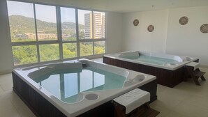 Ein Spa-Raum mit zwei Whirlpools, großen Fenstern und Blick auf eine Stadtlandschaft.