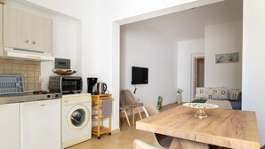A compact kitchen with a washing machine, microwave, and a small dining area with a wooden table and chairs. - Sinani Beachfront Gems Rhodes Jacuzzi Retreat (Rhodes)