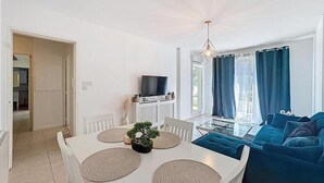 En moderne stue med et hvidt spisebord, blå sofa og et fjernsyn på et hvidt skab.