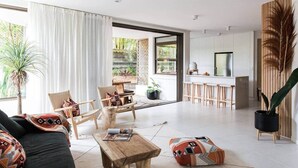 A modern living room with a sofa, chairs, a coffee table, and a dining area with a table and chairs. - Two Bedroom Beach Bungalow (Noosa Heads)