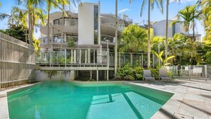 A swimming pool with a clear blue water, surrounded by palm trees and a modern building with balconies. - Two Bedroom Beach Bungalow (Noosa Heads)