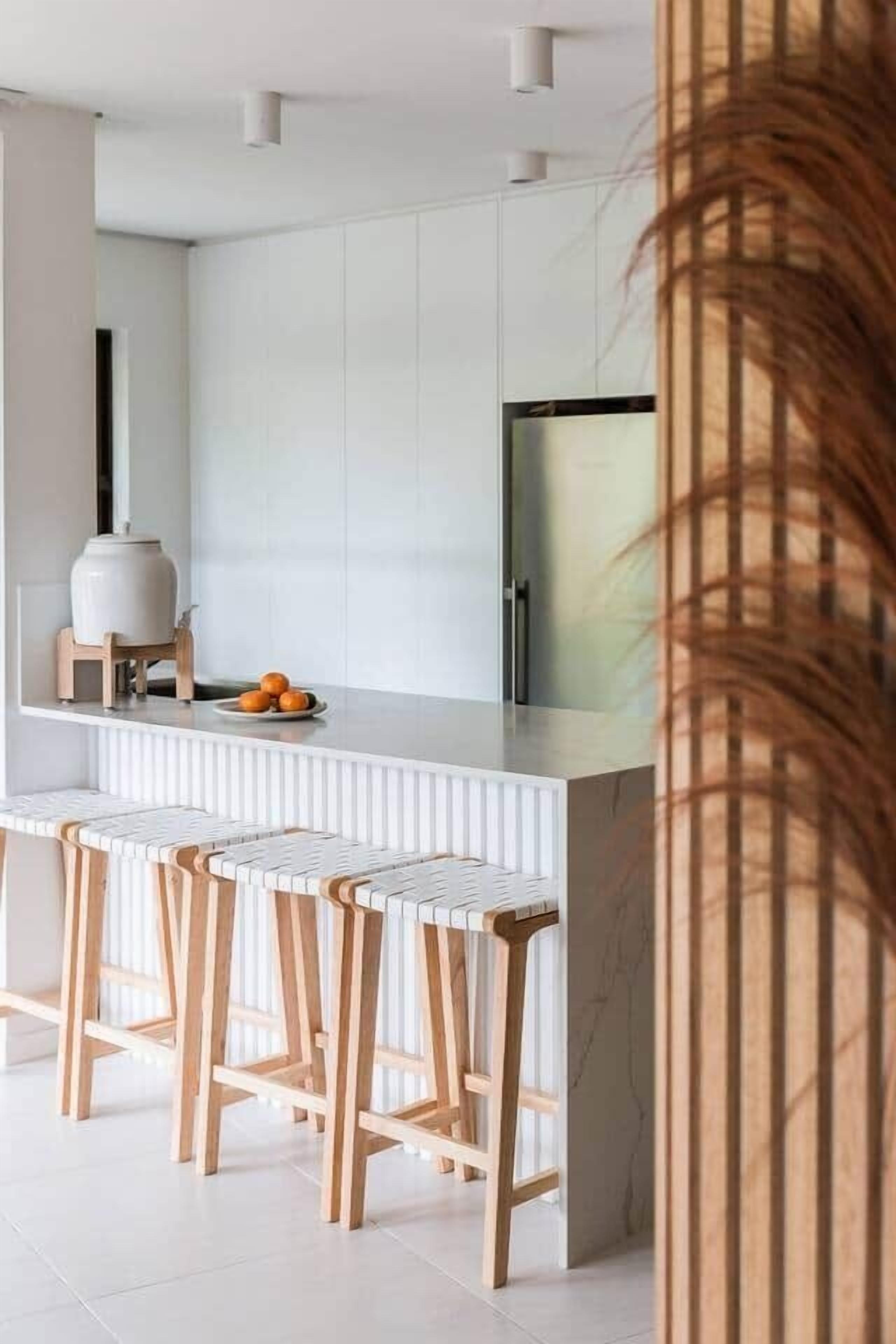 Una cocina moderna con armarios blancos, encimera de mármol y taburetes de madera.