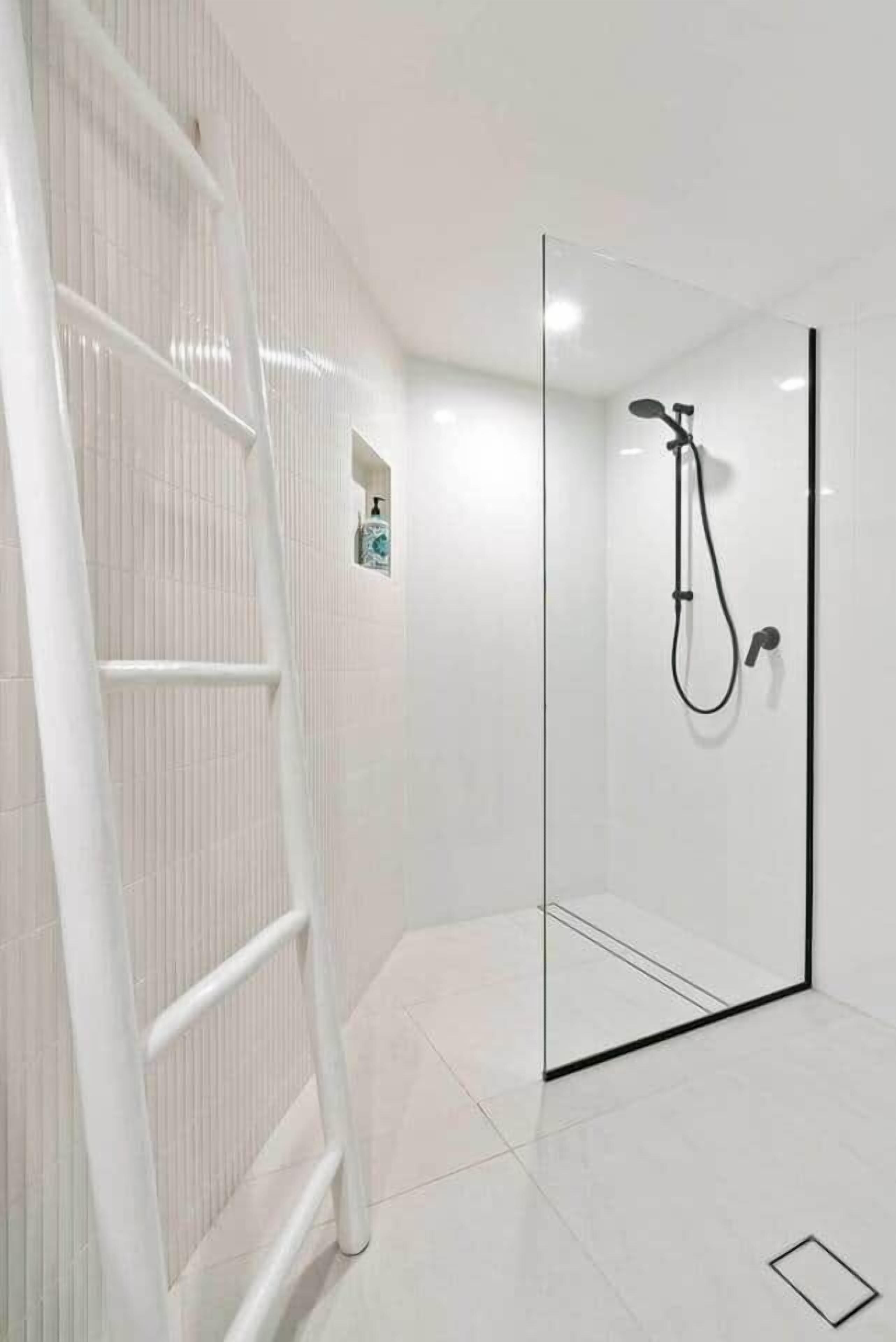 Un baño moderno con cabina de ducha de vidrio, suelo de azulejos blancos y una escalera blanca.