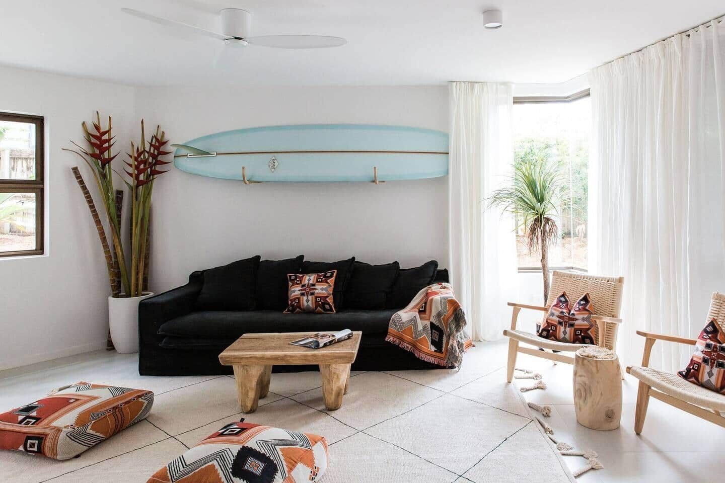 A living room with a black sofa, wooden coffee table, and a surfboard decoration on the wall.