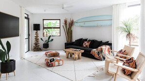 A living room with a black sofa, wooden coffee table, and wicker chairs. - Two Bedroom Beach Bungalow (Noosa Heads)