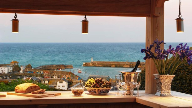A wooden bar with a view of the sea, a loaf of bread, a bowl of fruit, and a vase of flowers. - Breath-taking Estate With Pool Tennis Court Sea Views (St Austell)