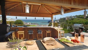 An outdoor kitchen with a view of the sea, a grill, and a variety of food items on the counter. - Breath-taking Estate With Pool Tennis Court Sea Views (St Austell)