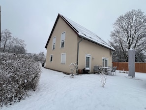 Ein zweistöckiges Haus mit schneebedecktem Dach und einer Terrasse mit Gartenmöbeln.