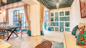 Un coin repas avec une table dressée pour quatre personnes, un canapé agrémenté de coussins colorés et un mur décoré de vases.