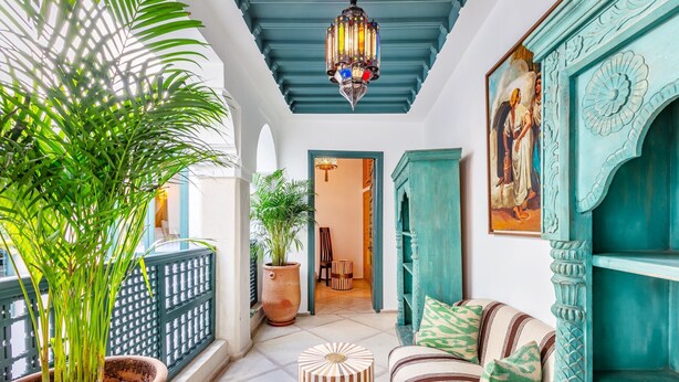 Une pièce avec une plante en pot, un canapé à rayures, un luminaire décoratif au plafond et une porte donnant sur une autre pièce.
