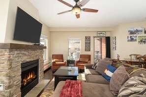 A living room with a fireplace, a flat-screen TV, a ceiling fan, and a couch.