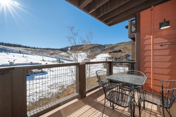 A balcony with a view of a snowy landscape, a table with chairs, and a metal railing. - NEW ski-in/ski-out 3 bedroom, private deck, views and plenty of bedding! (Granby)
