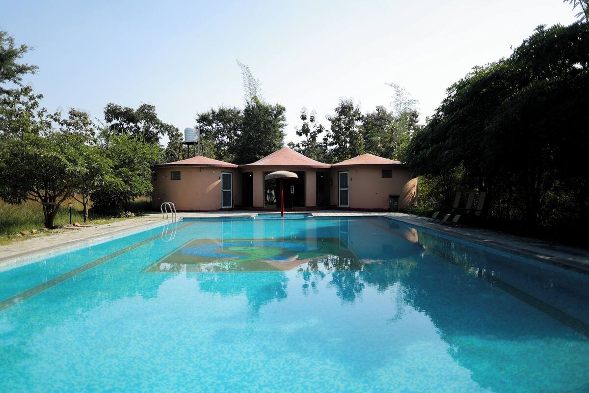 A swimming pool with a clear blue water surface, surrounded by trees and a building with a red roof.