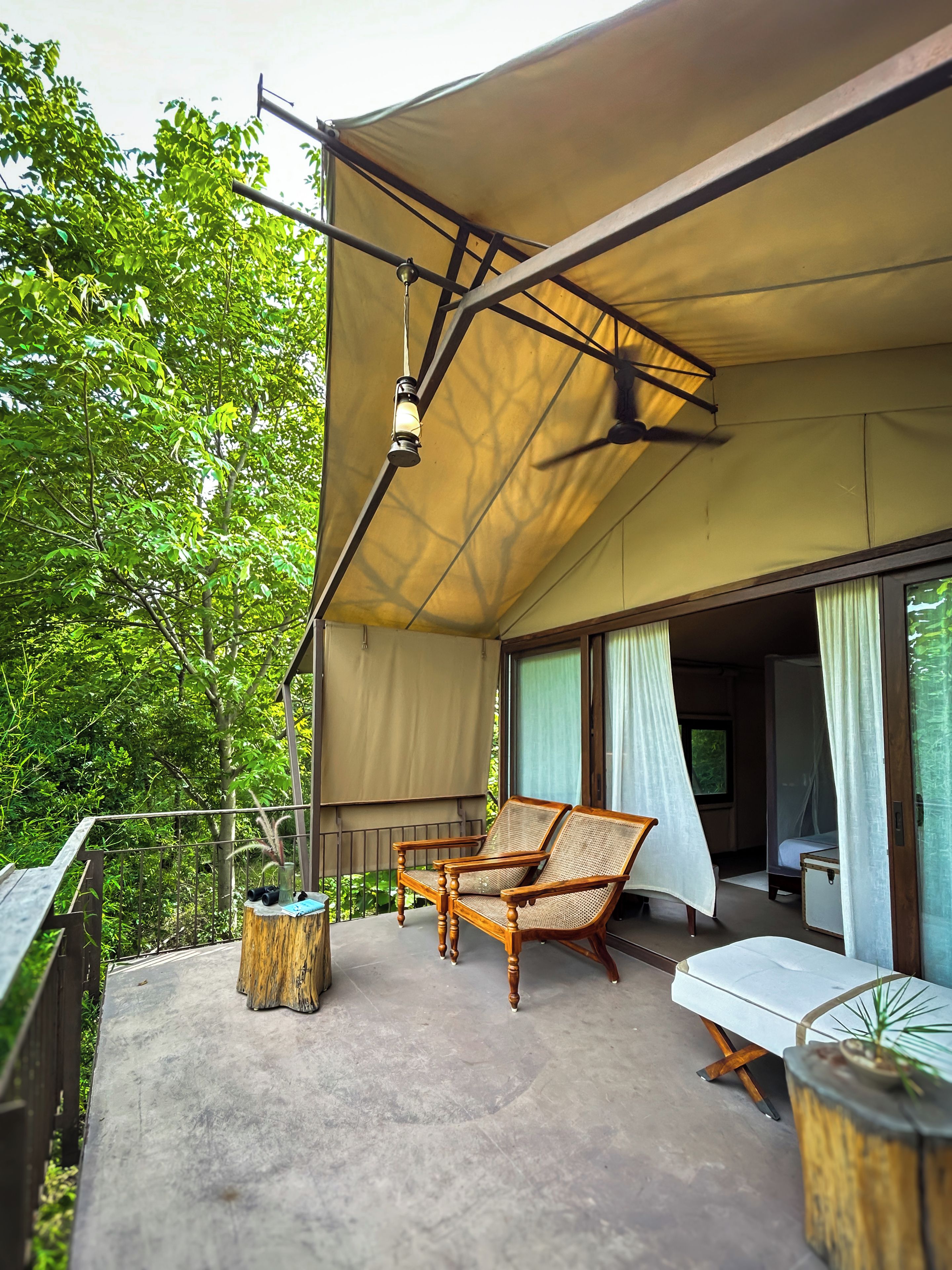 A balcony with a canopy, two wicker chairs, a small table, and a potted plant.