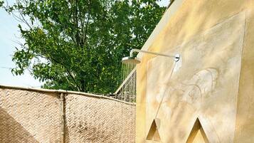 An outdoor shower area with a bamboo fence, a wooden deck, and a concrete wall with a water spout.