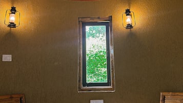 Habitación de esquina con una mesa de madera, dos sillas, un ventanal con vistas a zonas verdes y dos lámparas de pared.