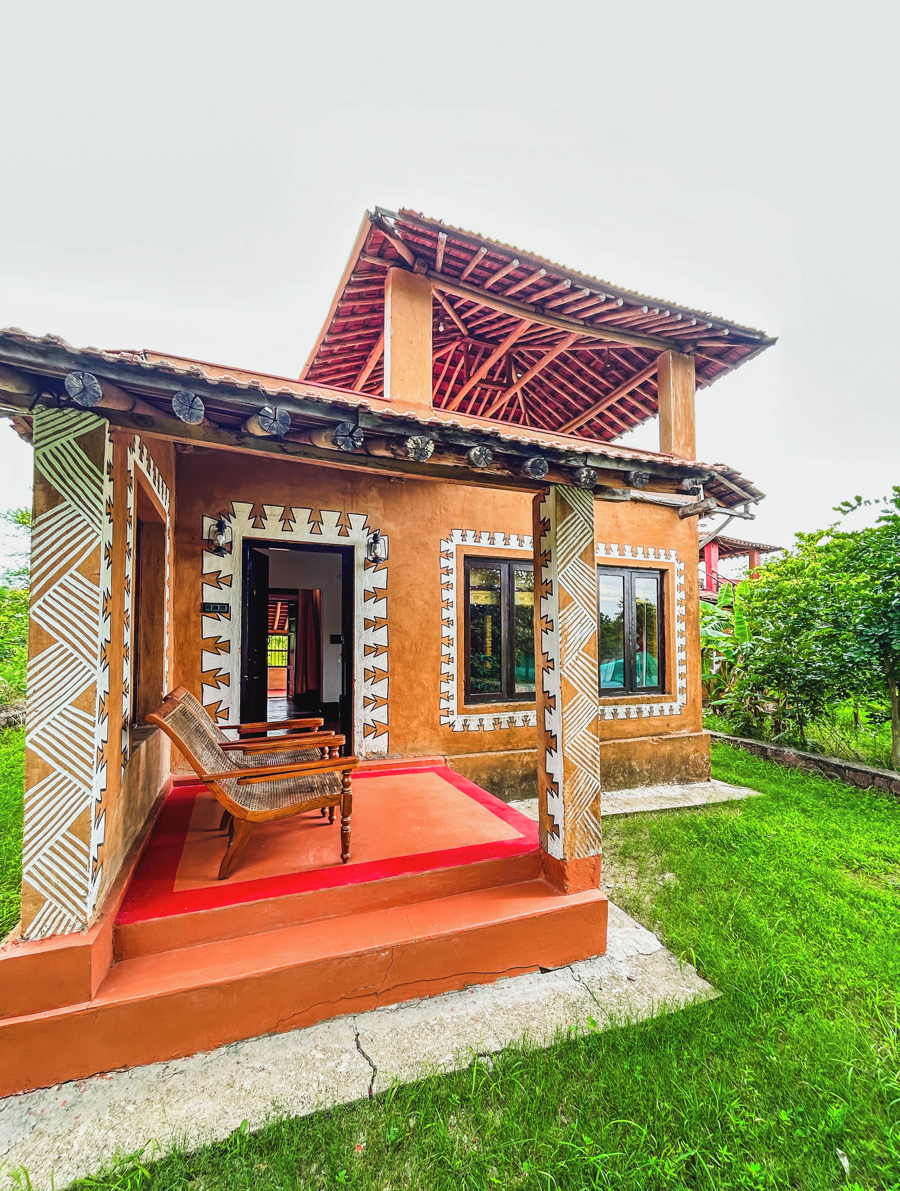 Una casa tradicional con techo rojo, un porche con banca de madera y ventana con vista a la vegetación.