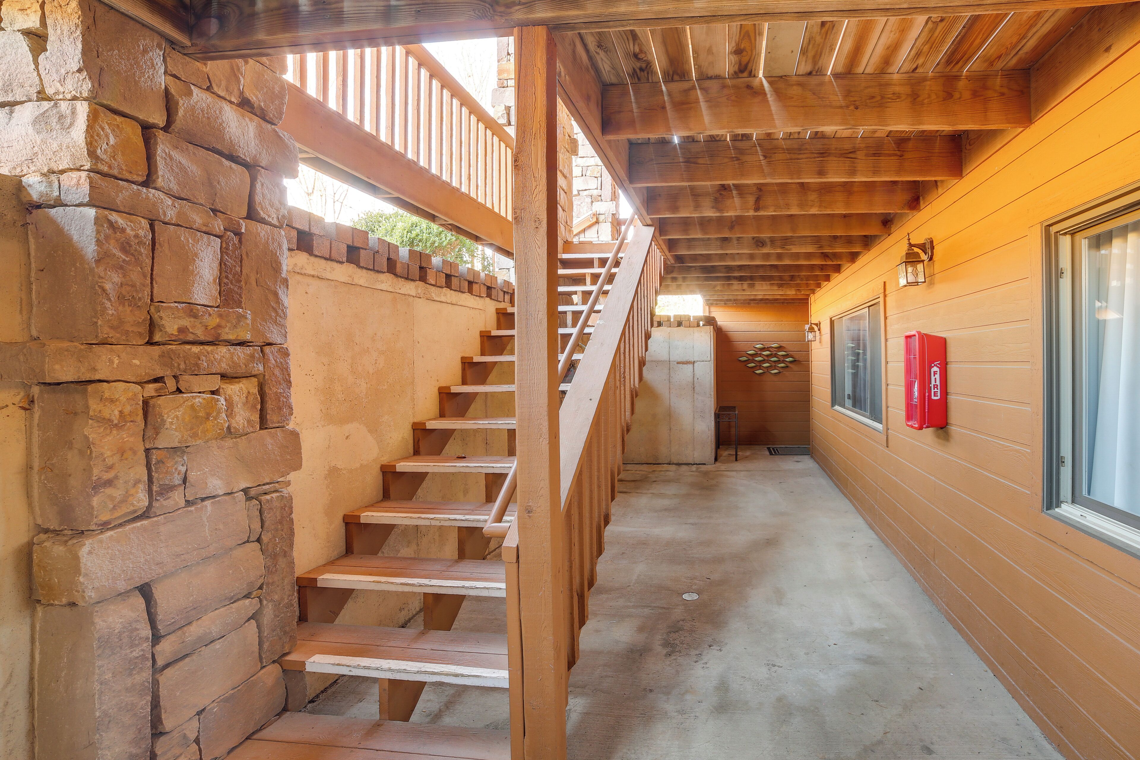 Una escalera de madera que sube a un segundo piso, una pared de piedra y una ventana con un extintor rojo en la pared.