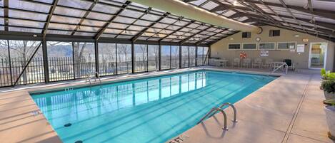 An indoor swimming pool with clear blue water, surrounded by a covered area with a metal roof and glass walls.