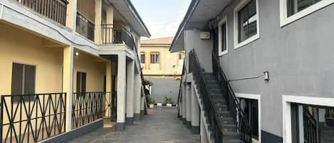 A narrow alleyway between buildings with a staircase on the right and a balcony on the left.
