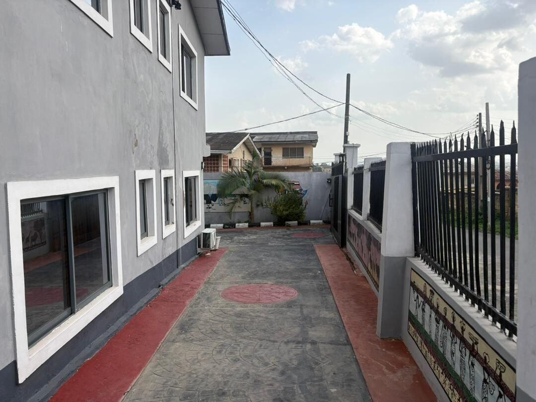 A narrow alleyway with a red-tiled path, a grey building with large windows, and a black metal fence.