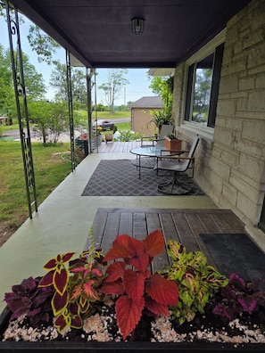 A covered porch with a table and chairs, a potted plant, and a view of the street.
