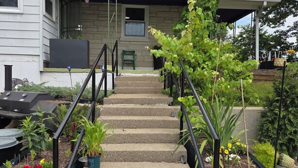 A house with a covered porch, a set of concrete stairs, and potted plants.