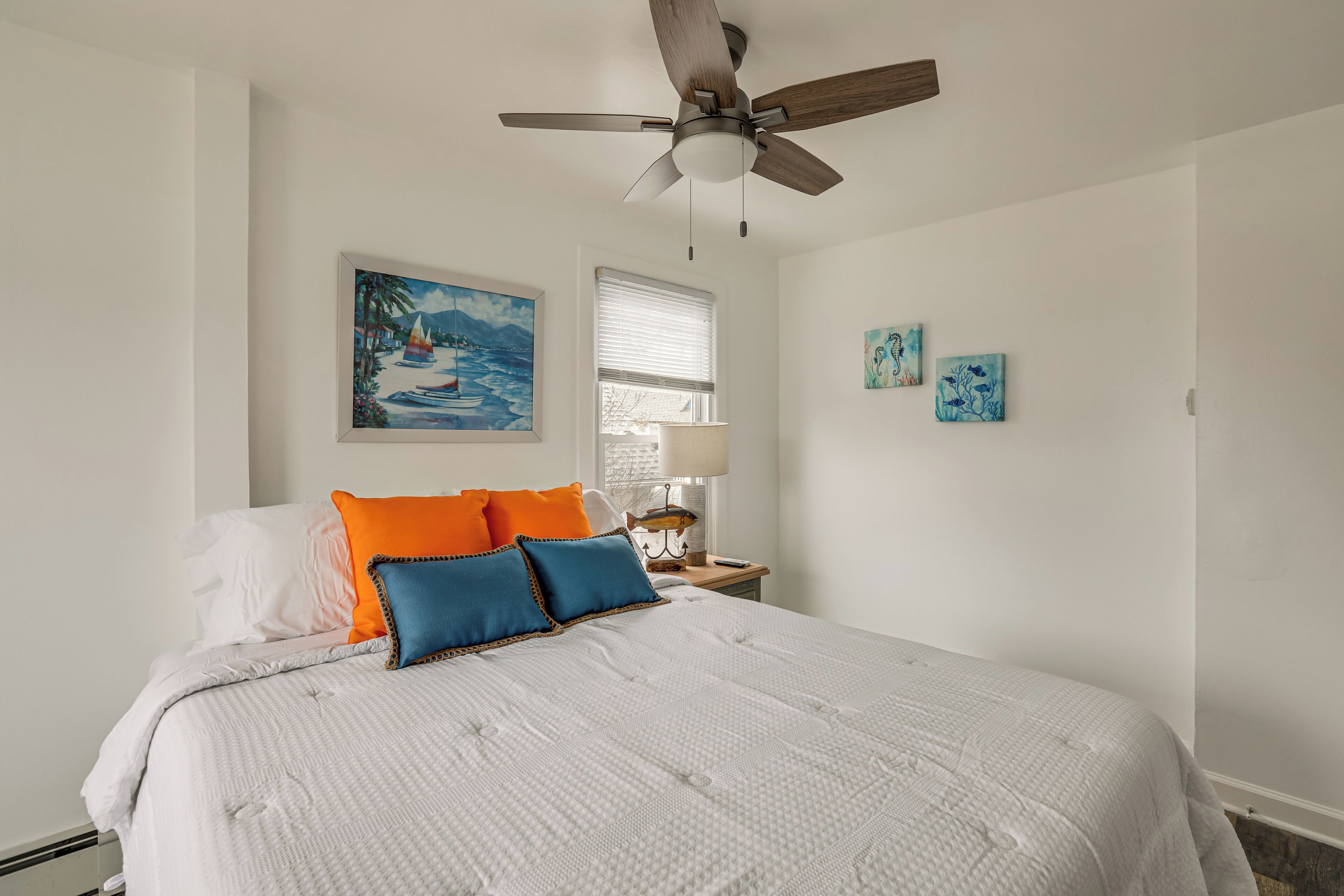 A bedroom with a bed, a ceiling fan, a window with blinds, and wall art.