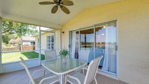 Une terrasse couverte avec une table et des chaises en verre, un ventilateur de plafond et une vue sur le jardin arrière.