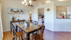 Un coin repas avec une table et des chaises en bois, un lustre et une cuisine en arrière-plan.